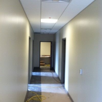 Empty office hallway with beige walls, gray carpet, and a yellow cord on the floor
