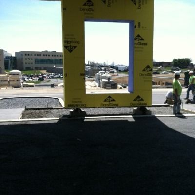 Yellow-framed opening at a construction site, with workers and vehicles visible outside in the background.