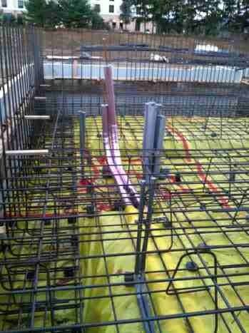Construction rebar grid with yellow insulation and vertical pipes on a building foundation
