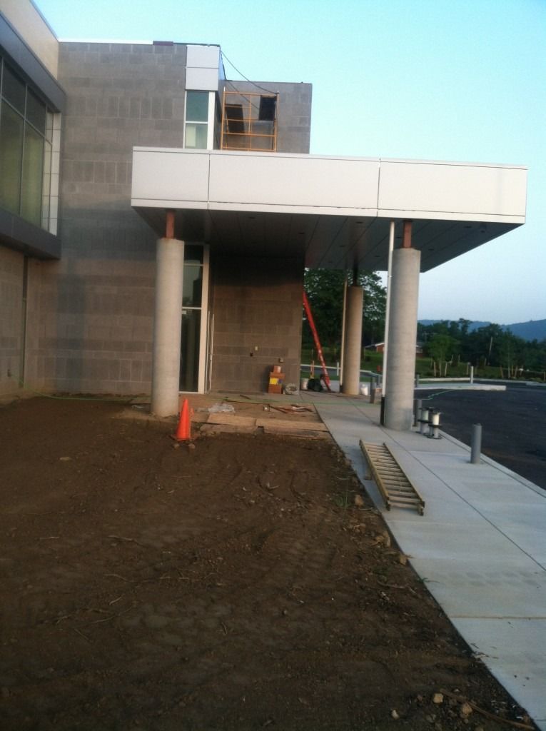 Modern building entrance with raised canopy, stairs, columns, and a sloped sidewalk at dusk