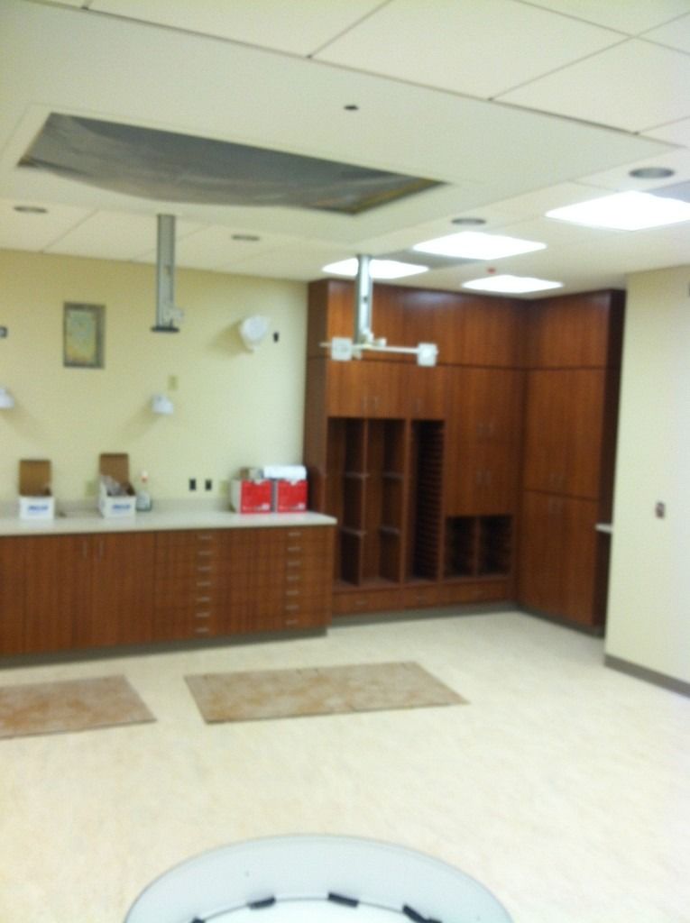 Empty office break room with cabinets, sinks, and ceiling tiles missing above.