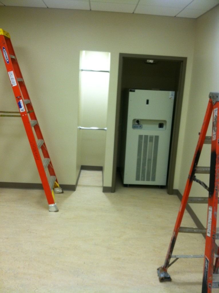 Room under renovation with two orange ladders flanking a wall niche and a white panel in an open doorway.