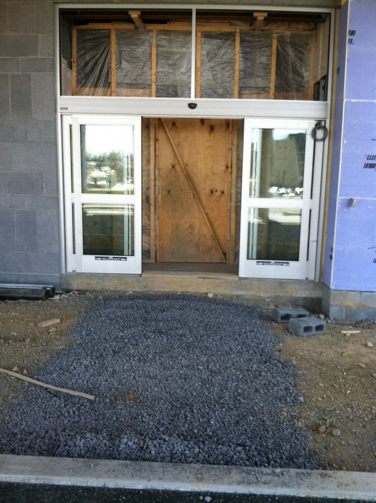 Storefront under construction with open glass doors and a boarded-up entrance.
