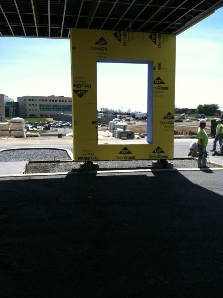 Large yellow construction frame under a canopy, with parked cars and a person walking in the background.