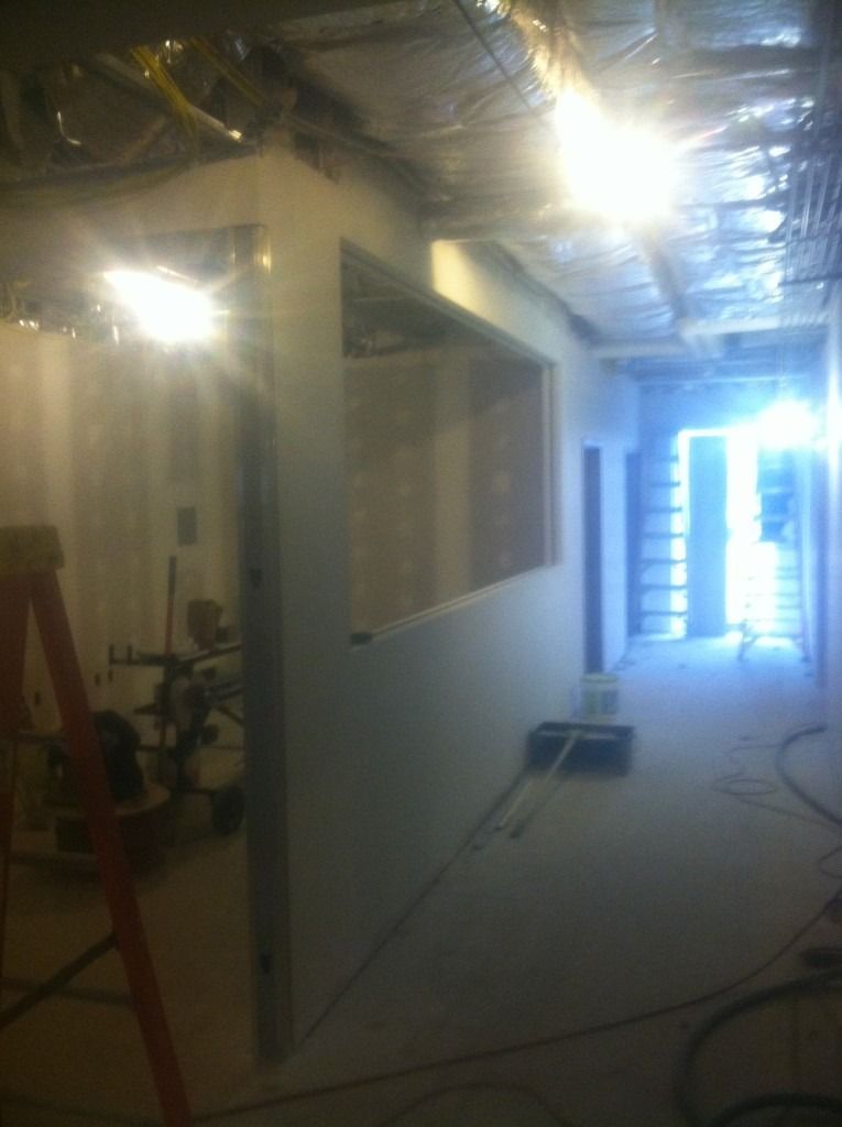 Unfinished hallway with exposed ceiling, bright light at the far end, and a ladder on the left.