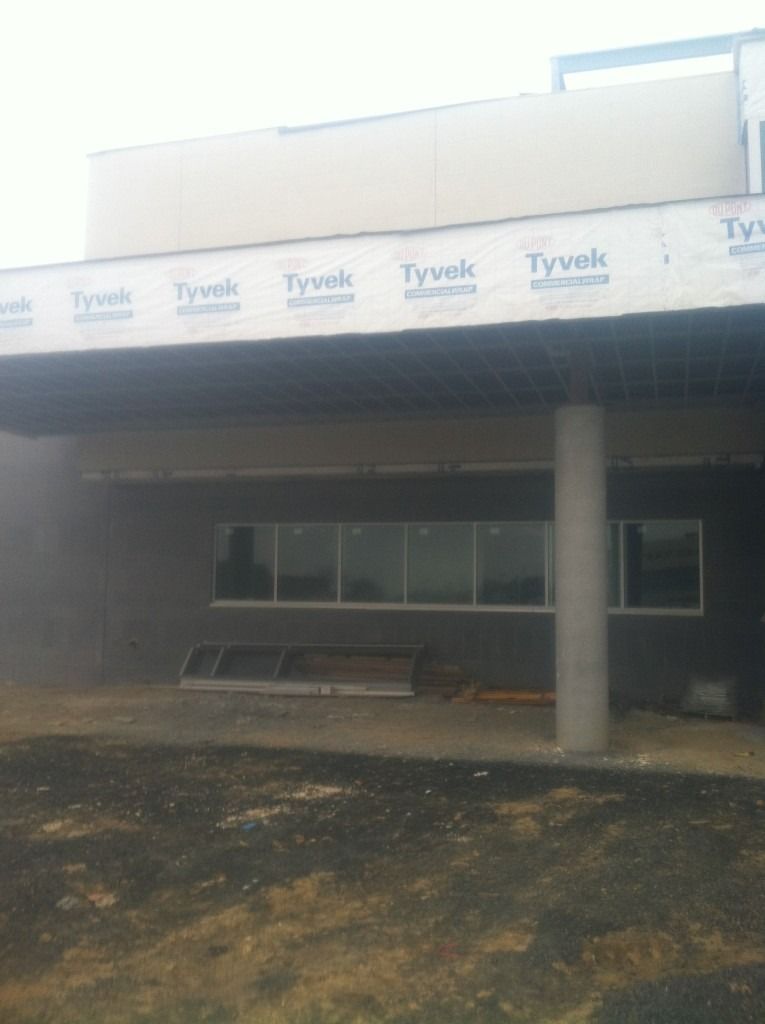 Exterior of a building under construction with Tyvek wrap, dark storefront, and a concrete column in front