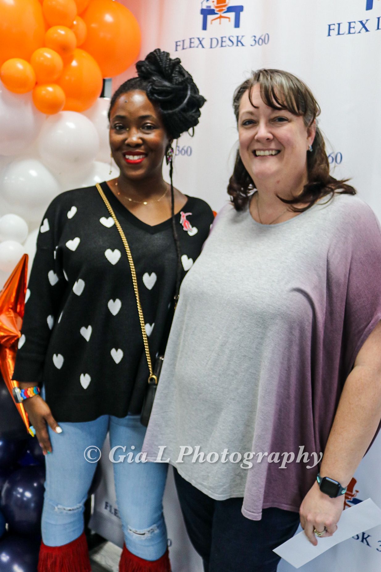 Two women standing next to each other in front of a flex desk 360 banner