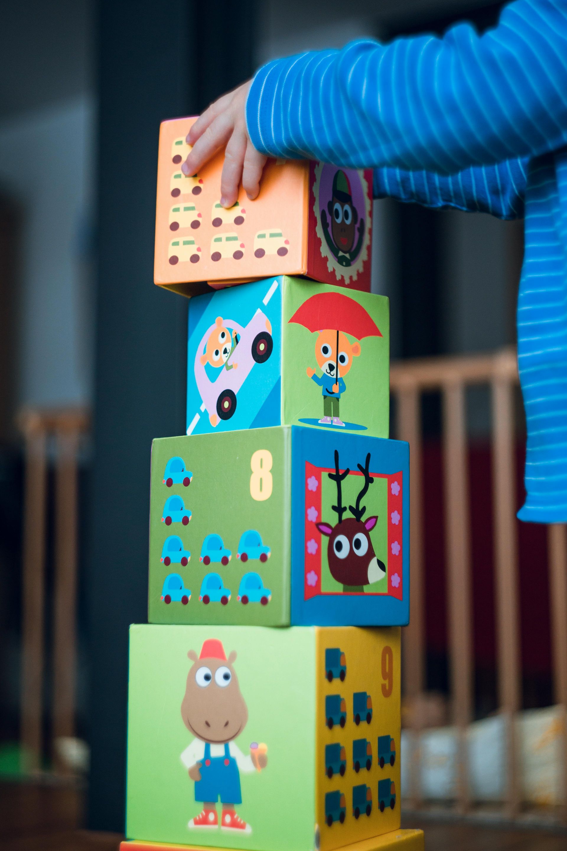 A child in daycare is stacking blocks with animals and numbers on them
