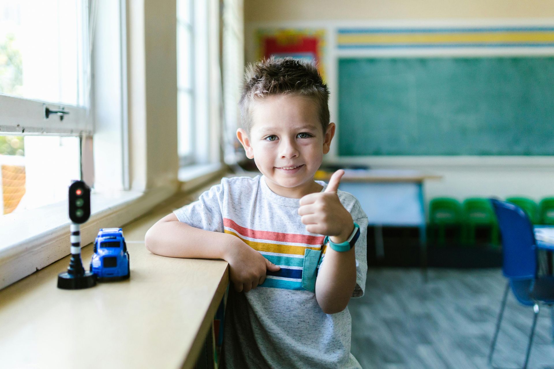 A young boy is giving a thumbs up in a classroom.