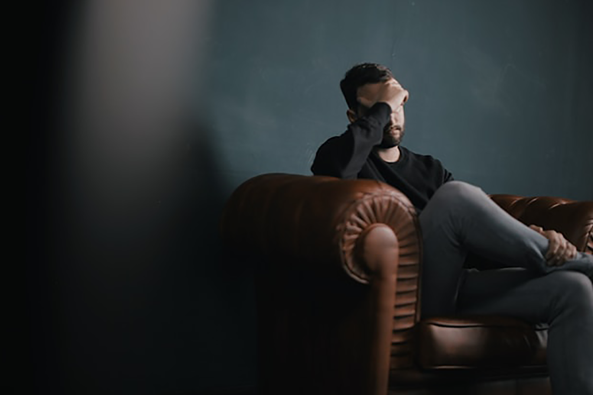 A man is sitting on a couch with his head in his hands.