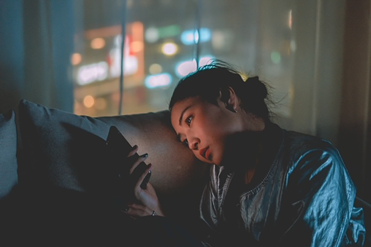 A woman is laying on a couch looking at her cell phone.