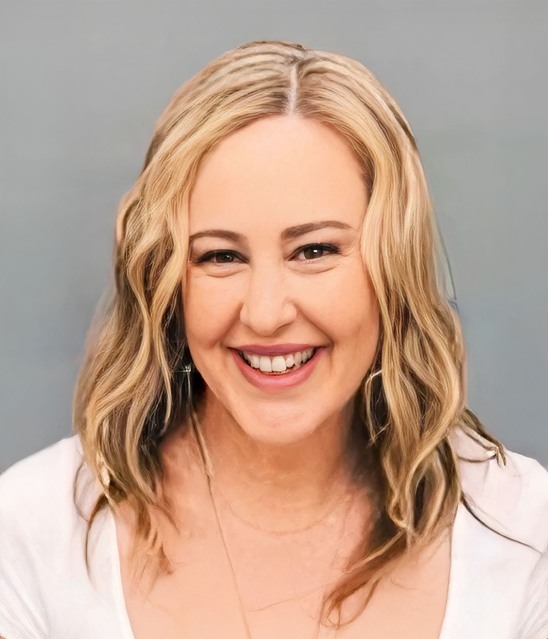 A woman with blonde hair is smiling and wearing a white shirt.