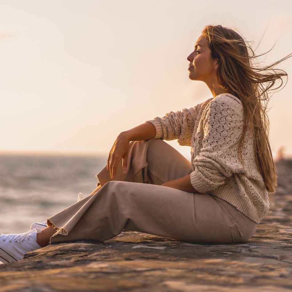A woman is sitting on the beach looking at the ocean.