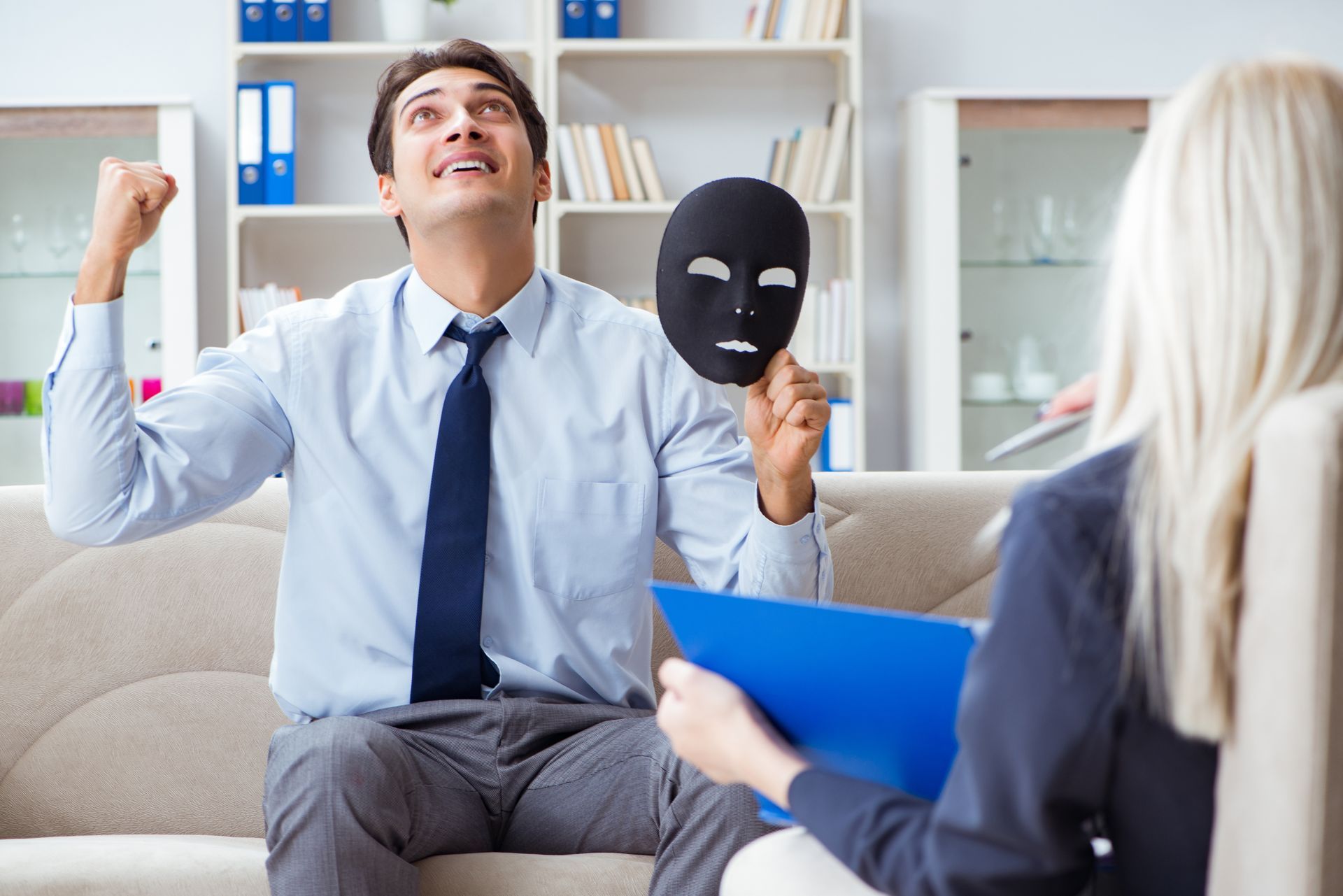 A man is sitting on a couch holding a mask in front of a woman.
