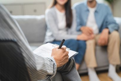 A man and a woman are sitting on a couch talking to a counselor.