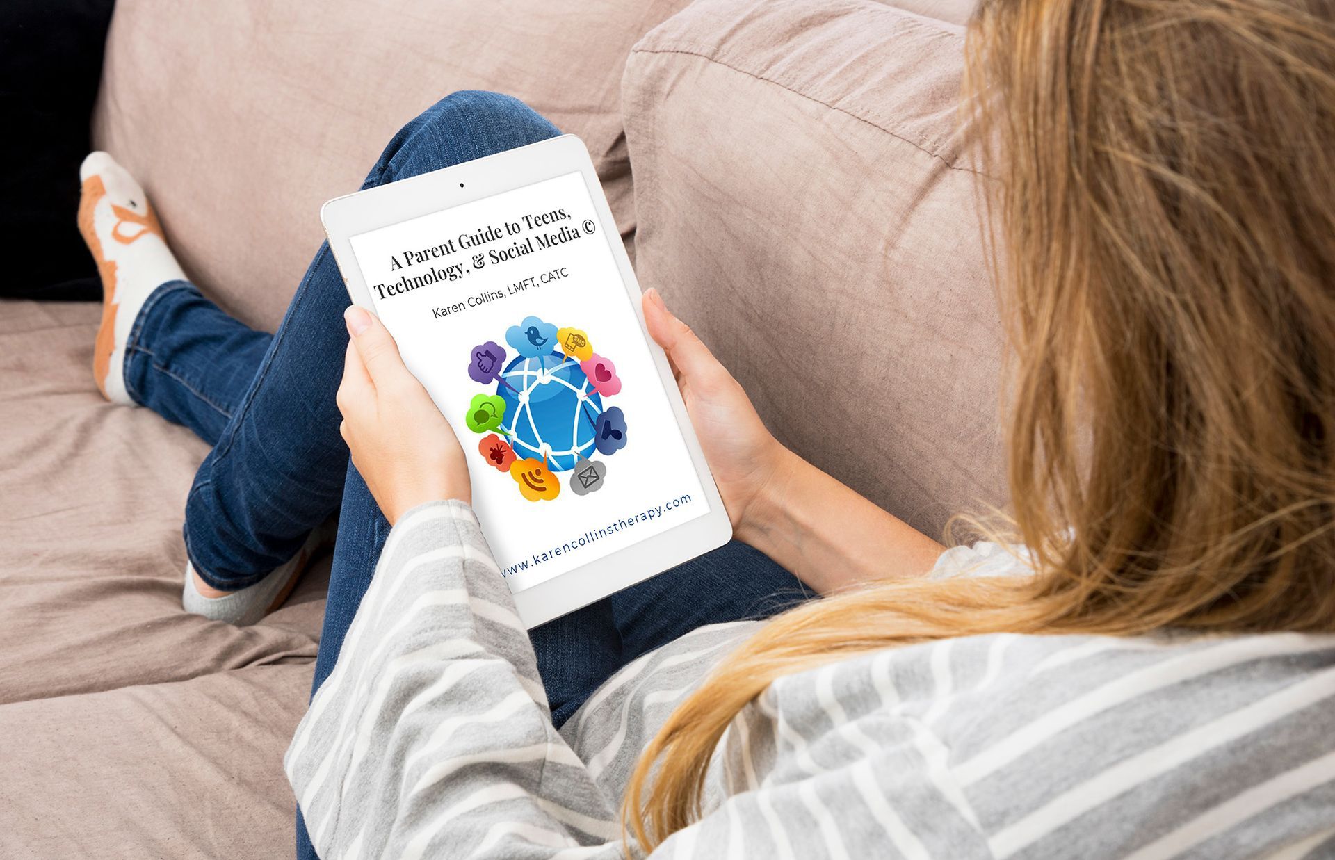 A woman is sitting on a couch holding a tablet.