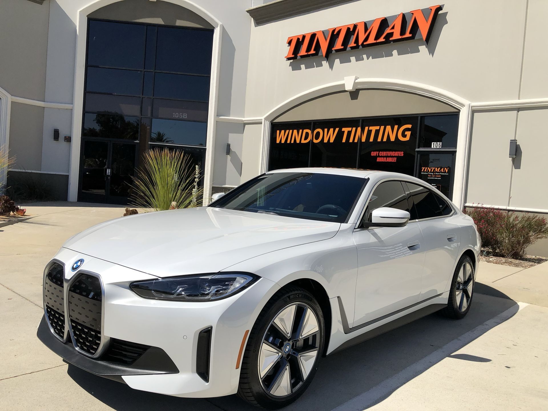 A white car is parked in front of a window tinting store.