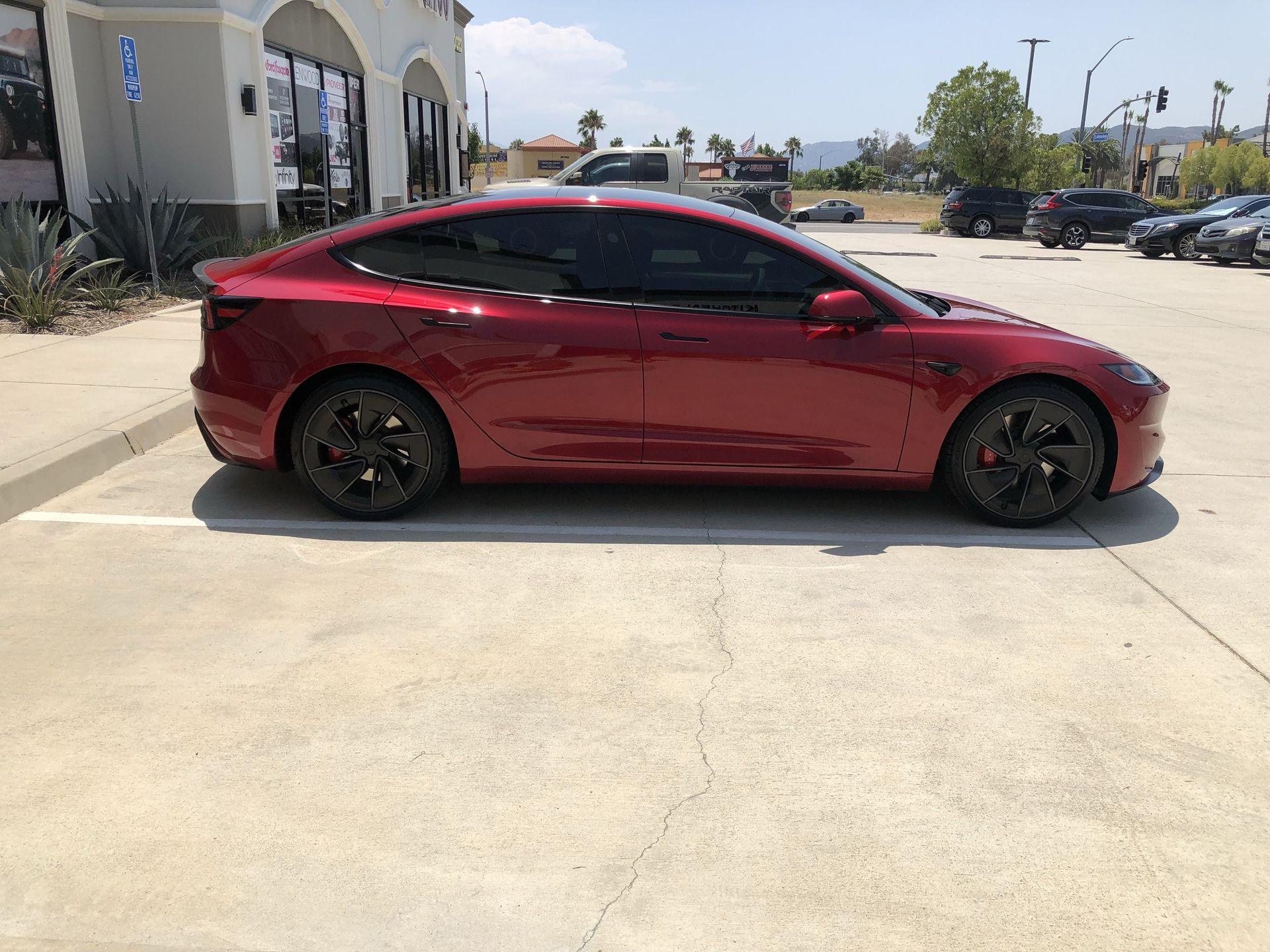 A red tesla model 3 is parked in a parking lot.
