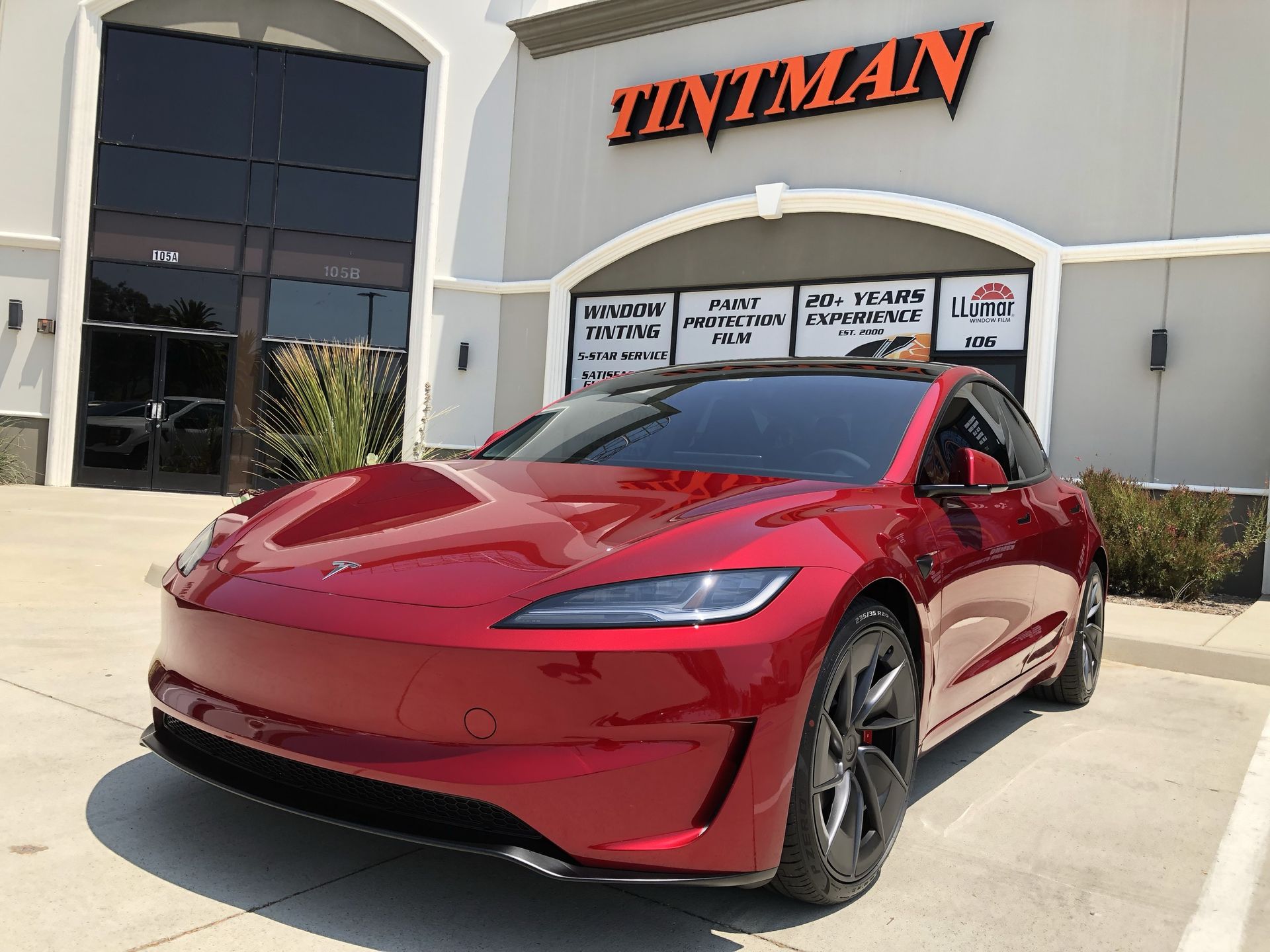 A red tesla model s is parked in front of a tintman store.
