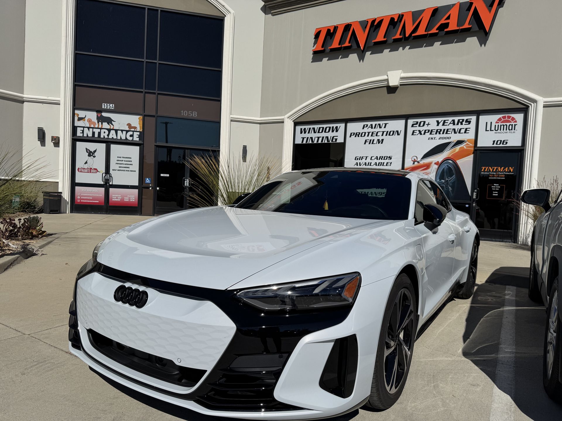 A white car is parked in front of a tintman store.