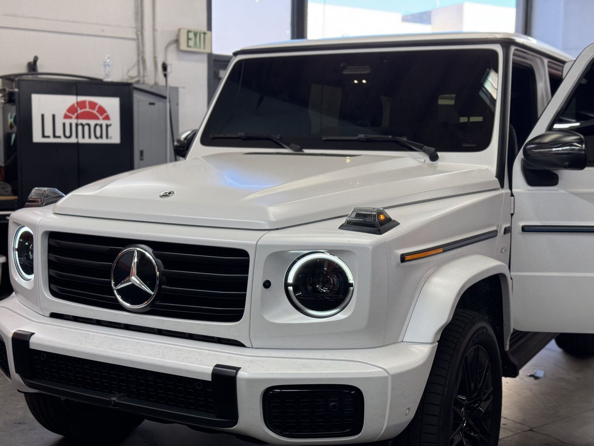 A white mercedes benz g class is parked in a garage with its doors open.