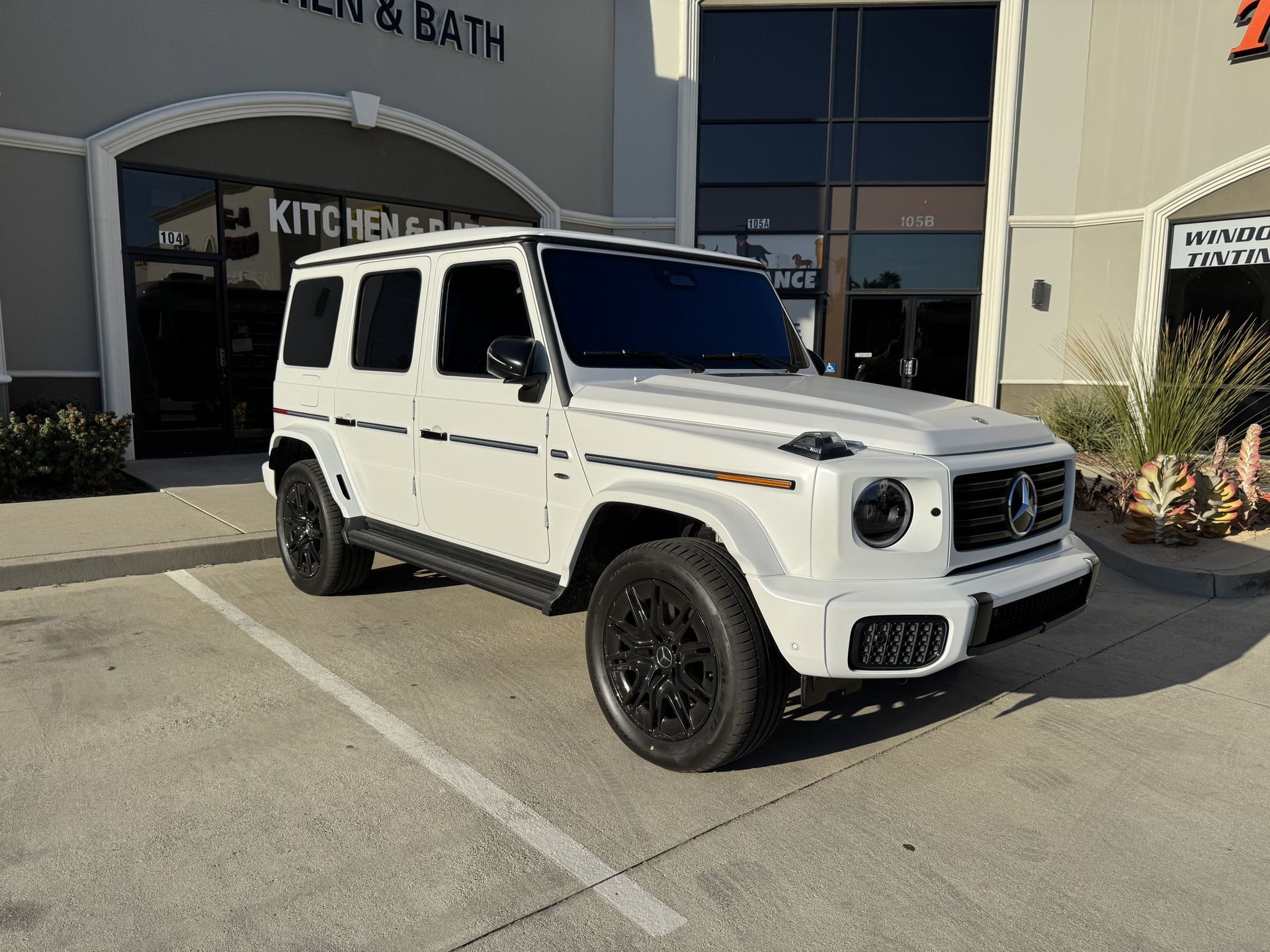 A white mercedes benz g class is parked in a parking lot in front of a building.