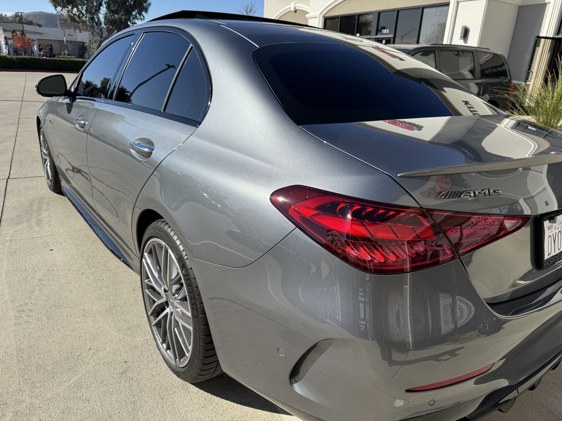 A gray car with a red tail light is parked in a parking lot.