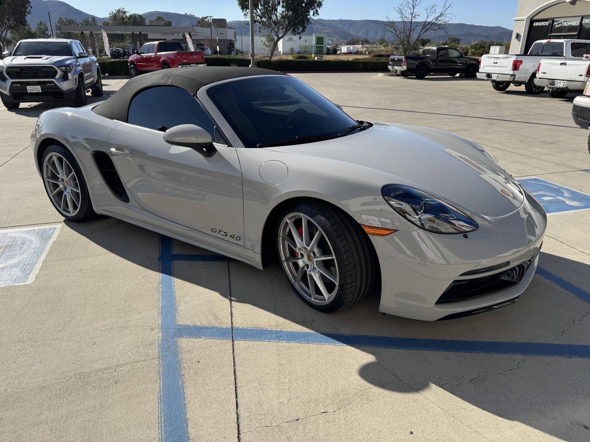 A white porsche boxster convertible is parked in a parking lot.