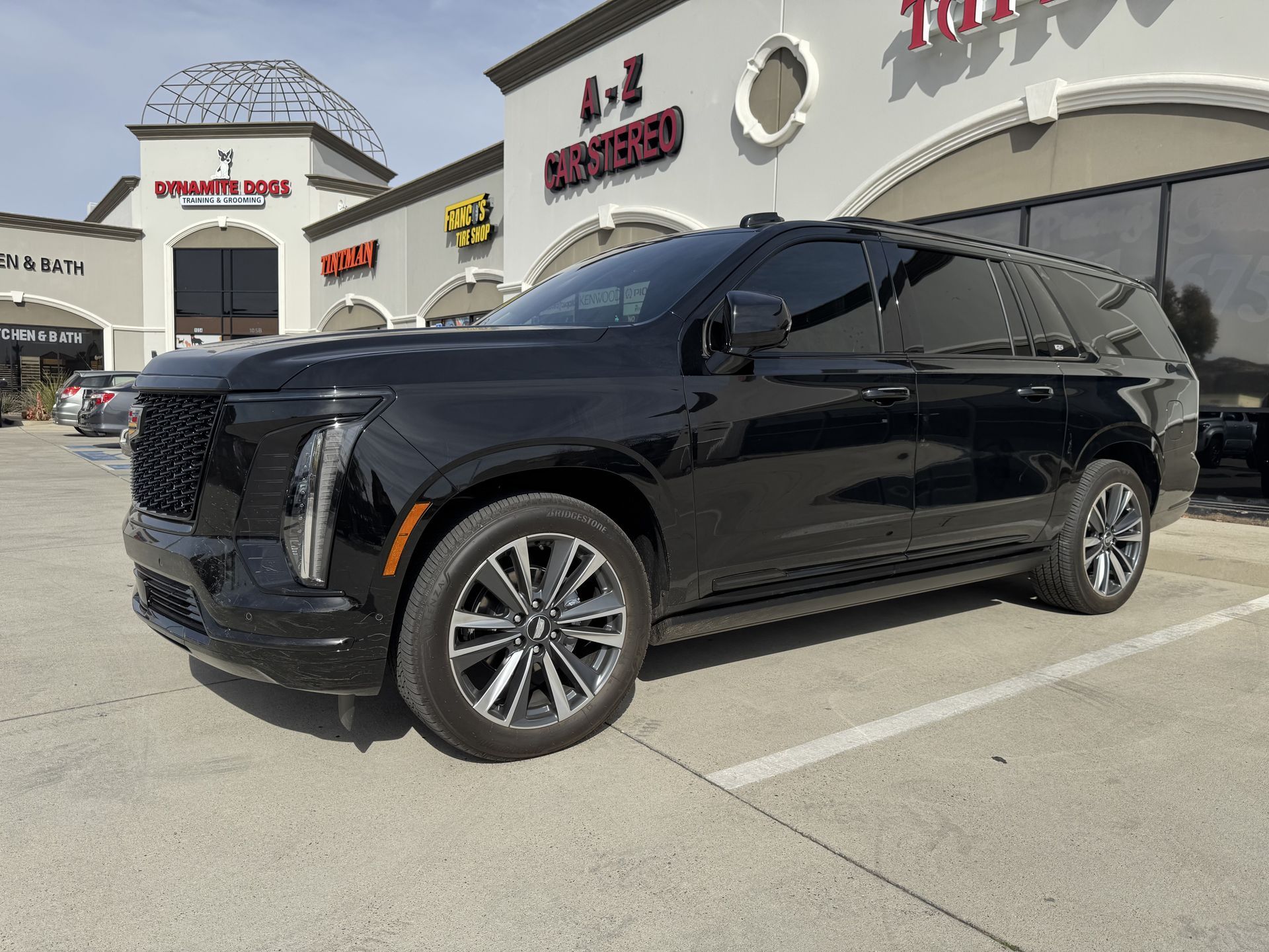 A black cadillac escalade is parked in a parking lot in front of a building.