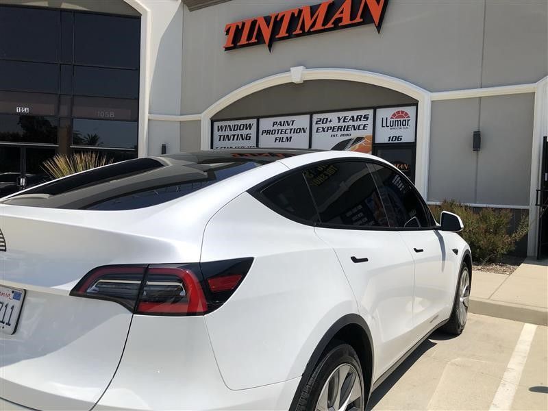 A white tesla model y is parked in front of a tintman store