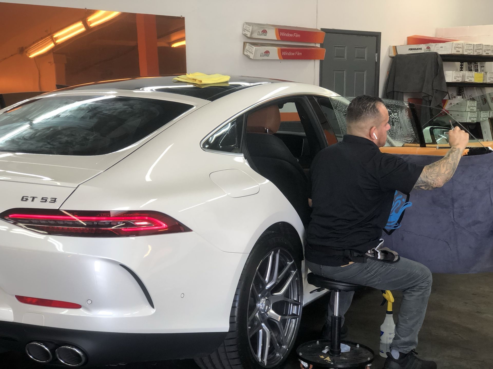 A man is sitting on a stool next to a white car