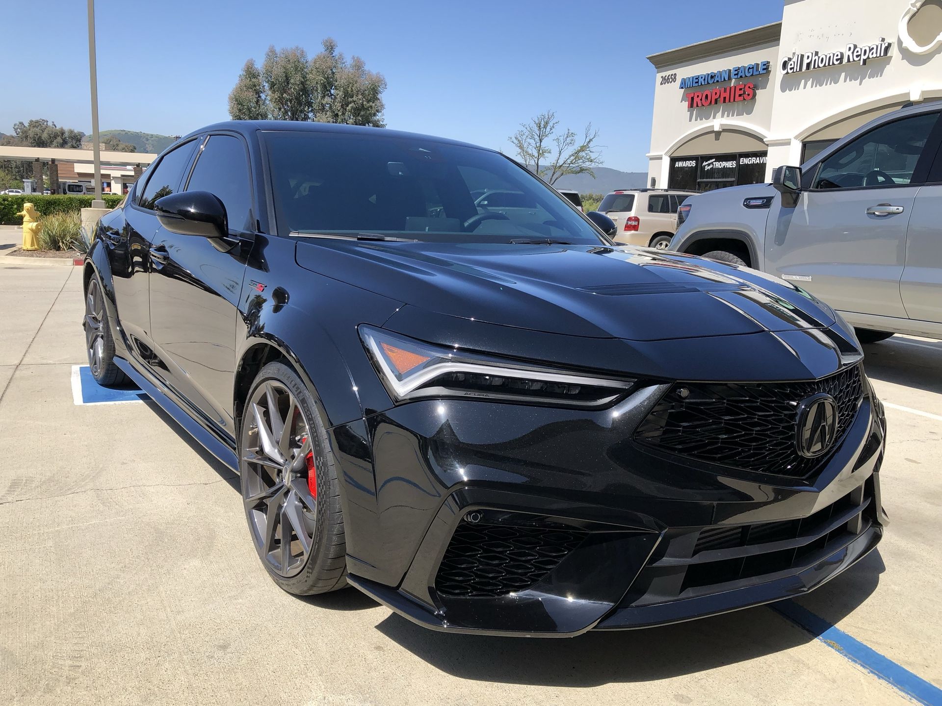 A black car is parked in a parking lot in front of a building.