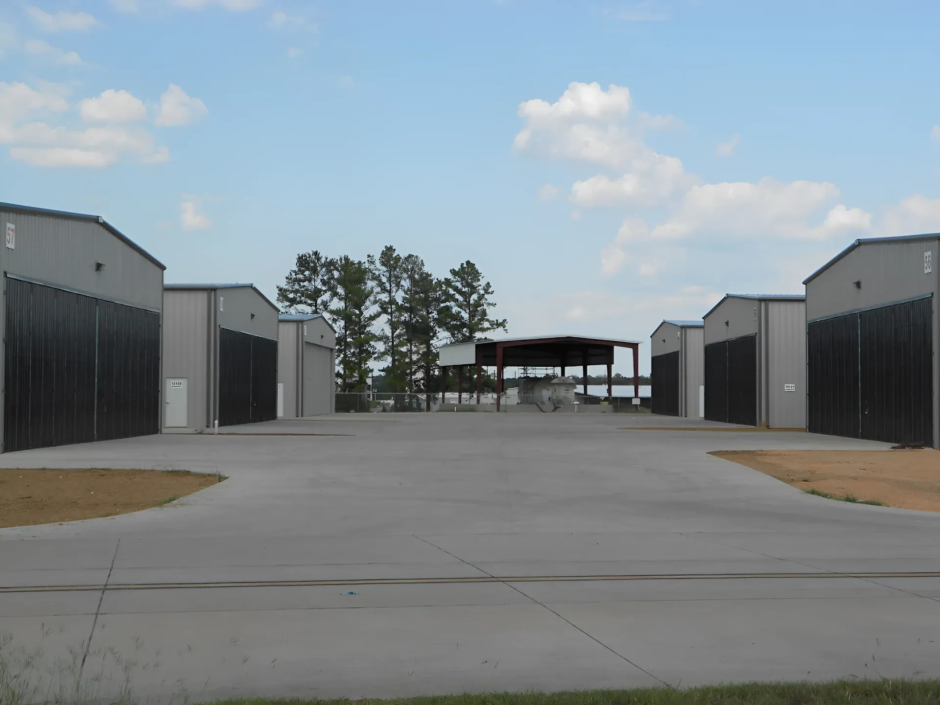 Rows of gray metal storage units face a concrete lot, with a few trees and blue sky visible in the background.