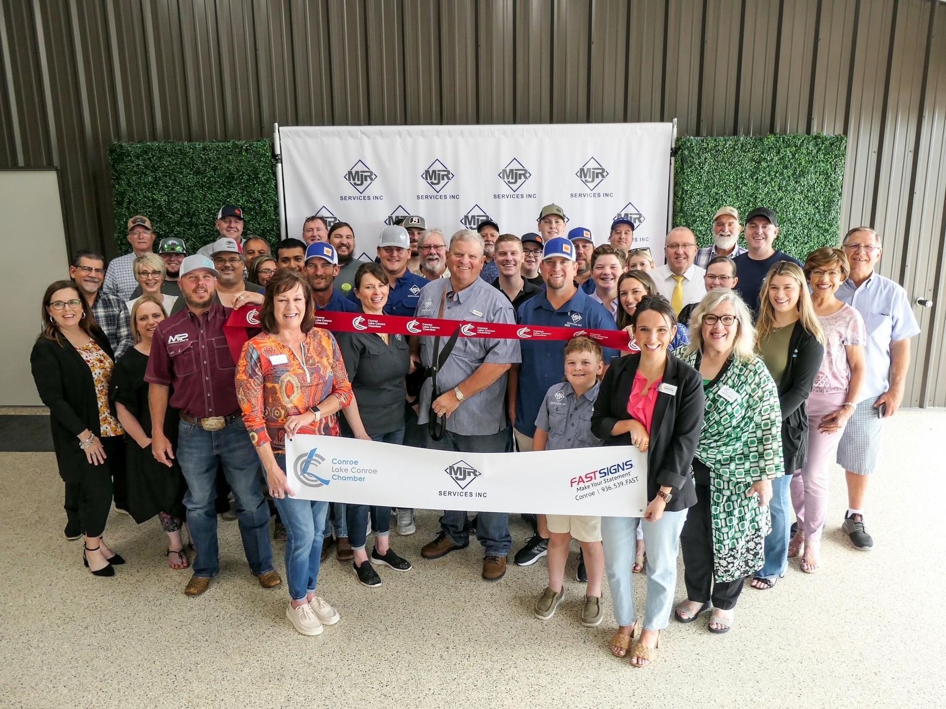 Group of people cutting a ribbon in front of a banner; likely a grand opening.