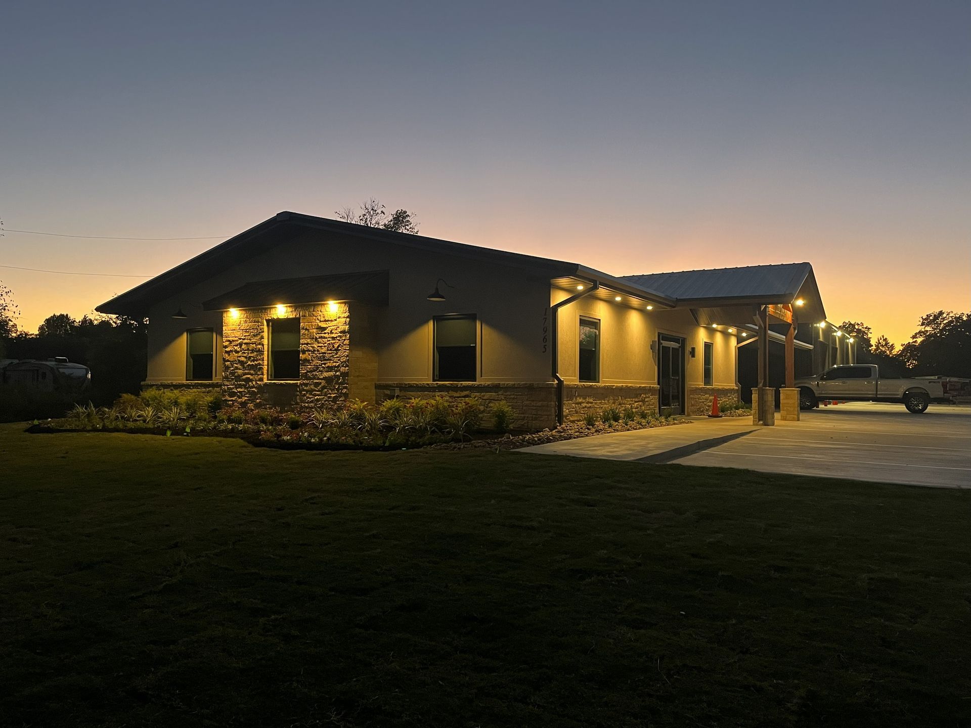 House exterior at dusk, with stone accents, illuminated windows, and a covered entryway.