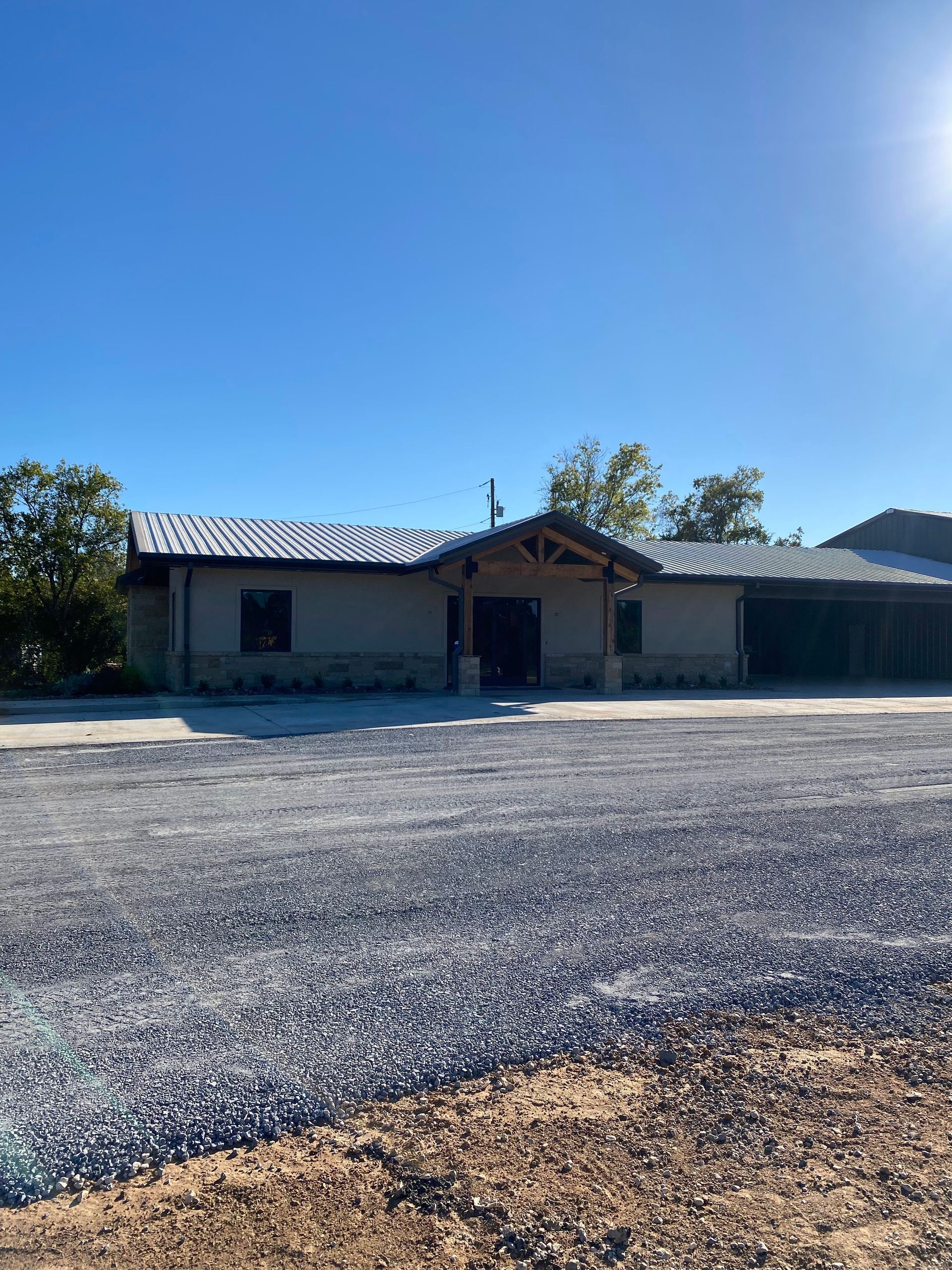 A single-story building with a gravel parking lot under a bright blue sky.