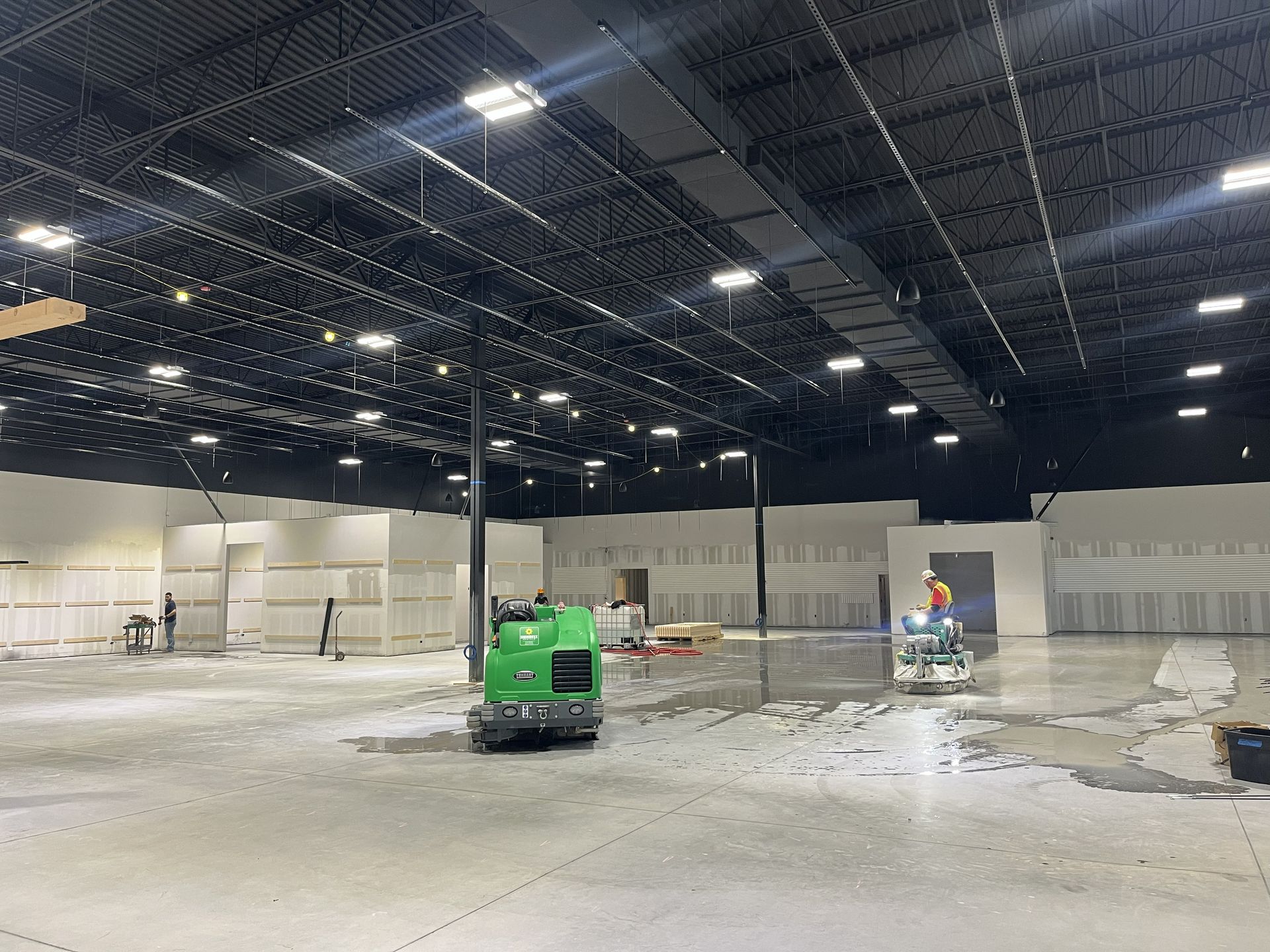 Construction site interior with exposed ceiling, concrete floor, workers, and machinery.