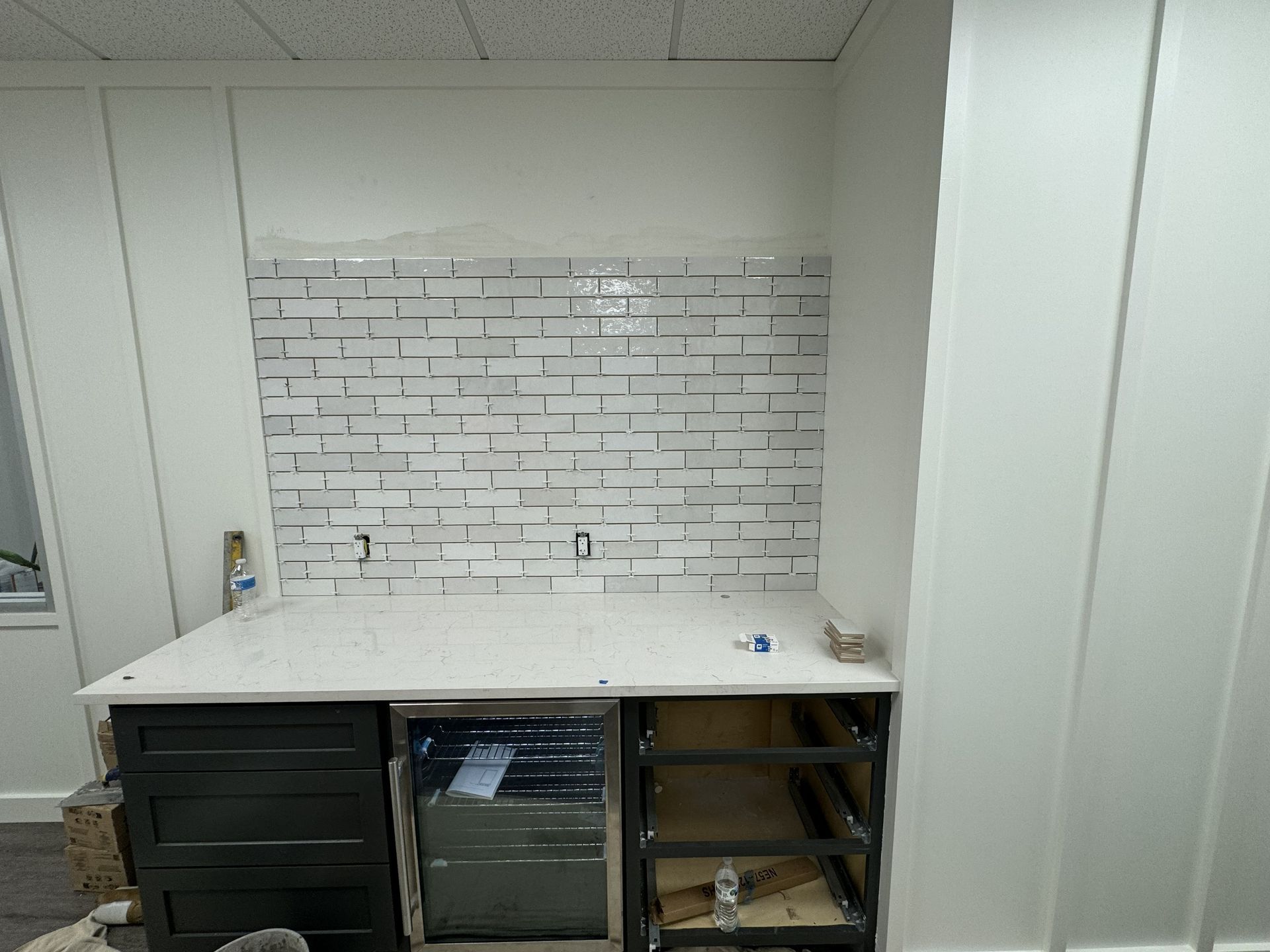 White kitchen countertop with white brick backsplash under construction. Cabinets and drawers are visible.