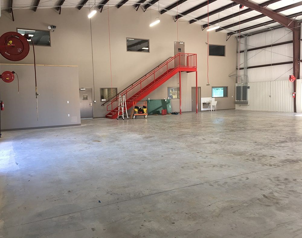 Large empty industrial building with concrete floor, red staircase, and high ceiling.