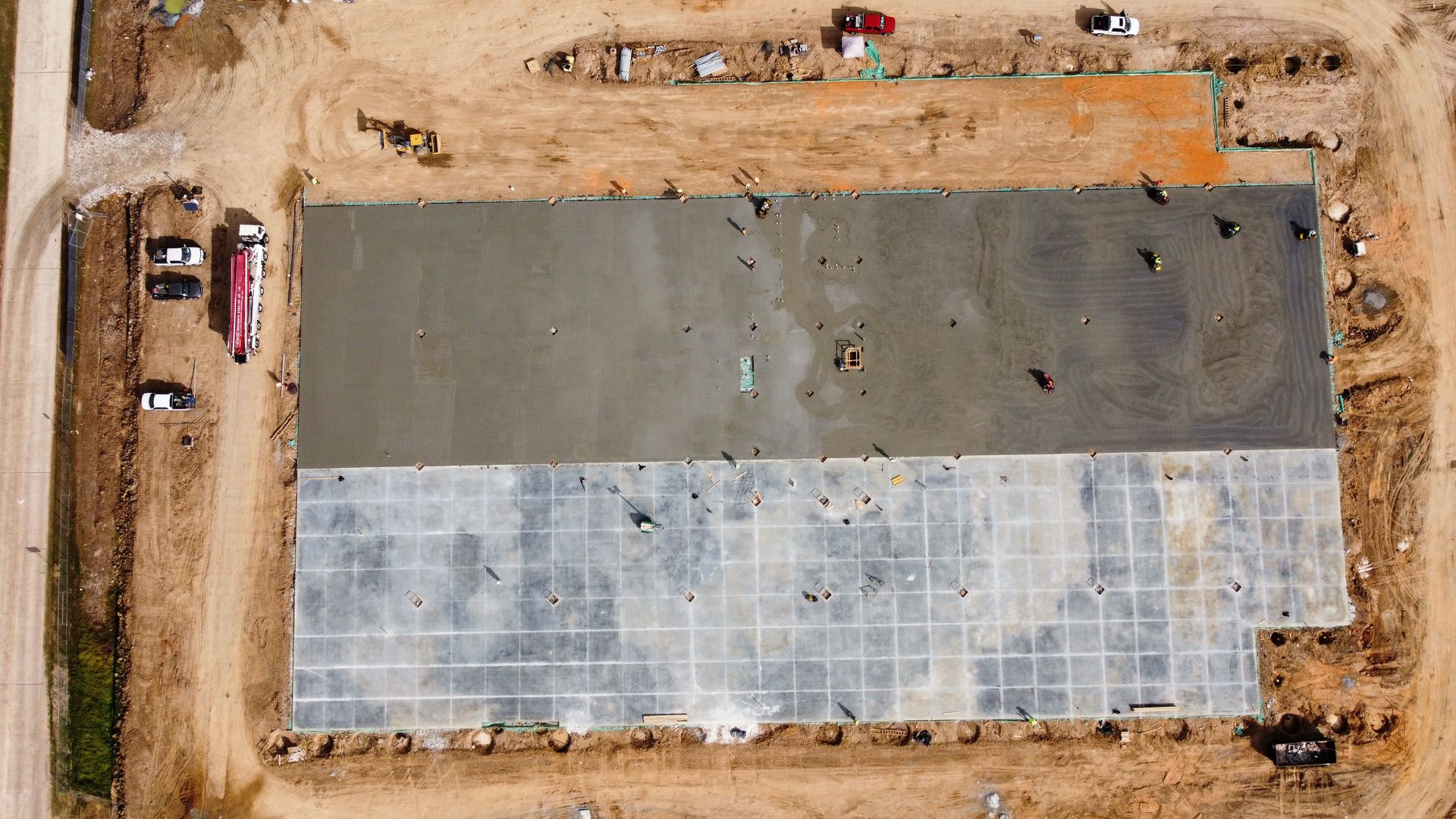 Aerial view of a construction site with concrete foundation, partially poured, dirt surrounding.