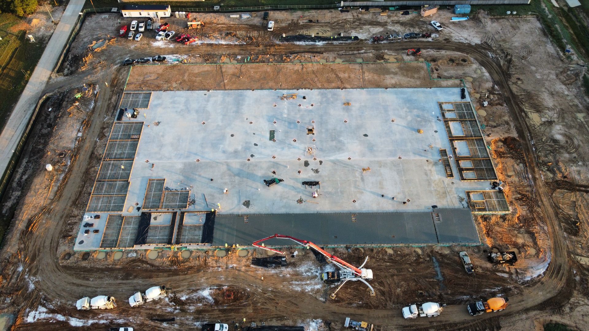 Aerial view of a large concrete foundation under construction; with trucks, machinery, and dirt surrounding.