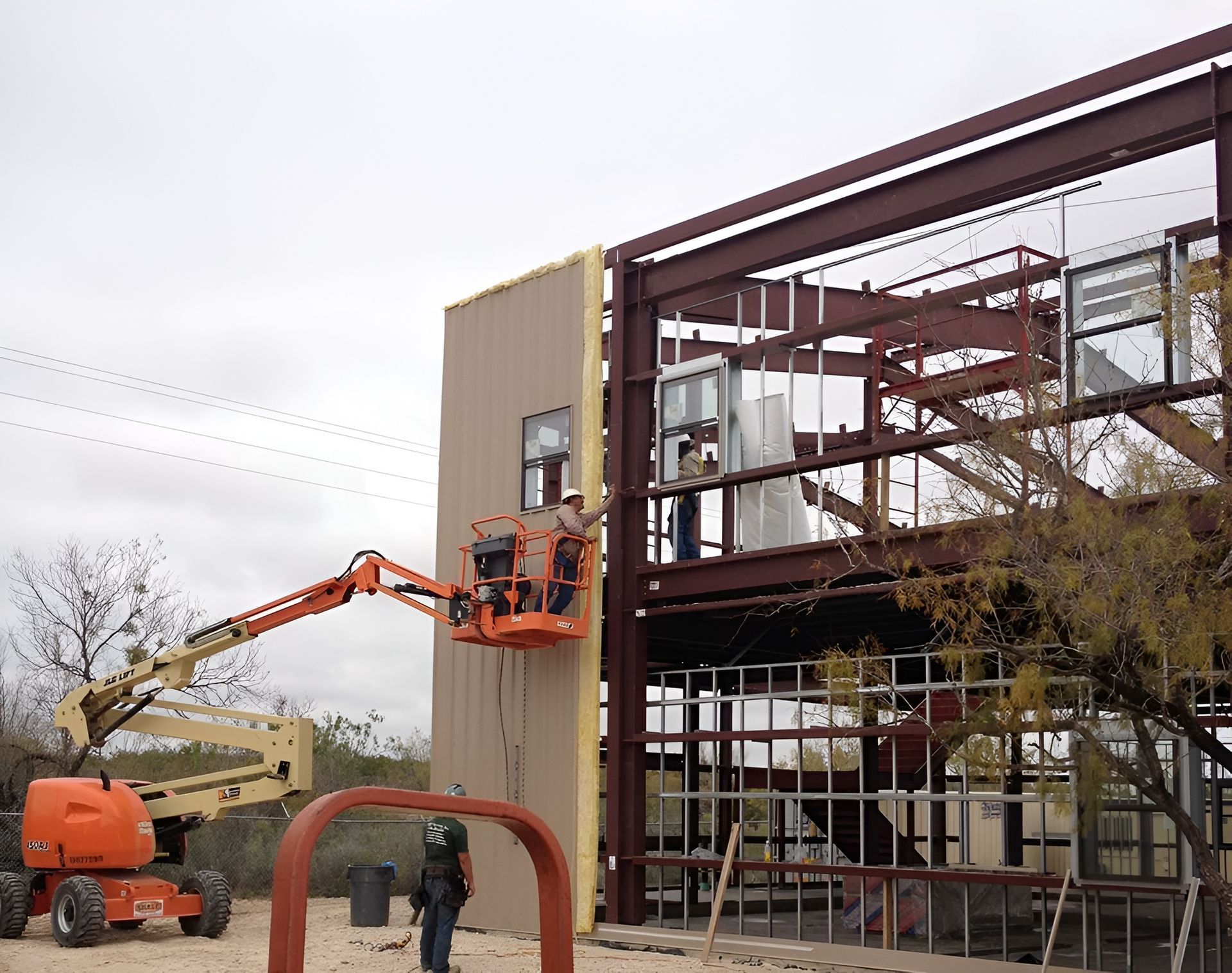 Construction site: A worker in a lift installs wall panels onto a steel-framed building.