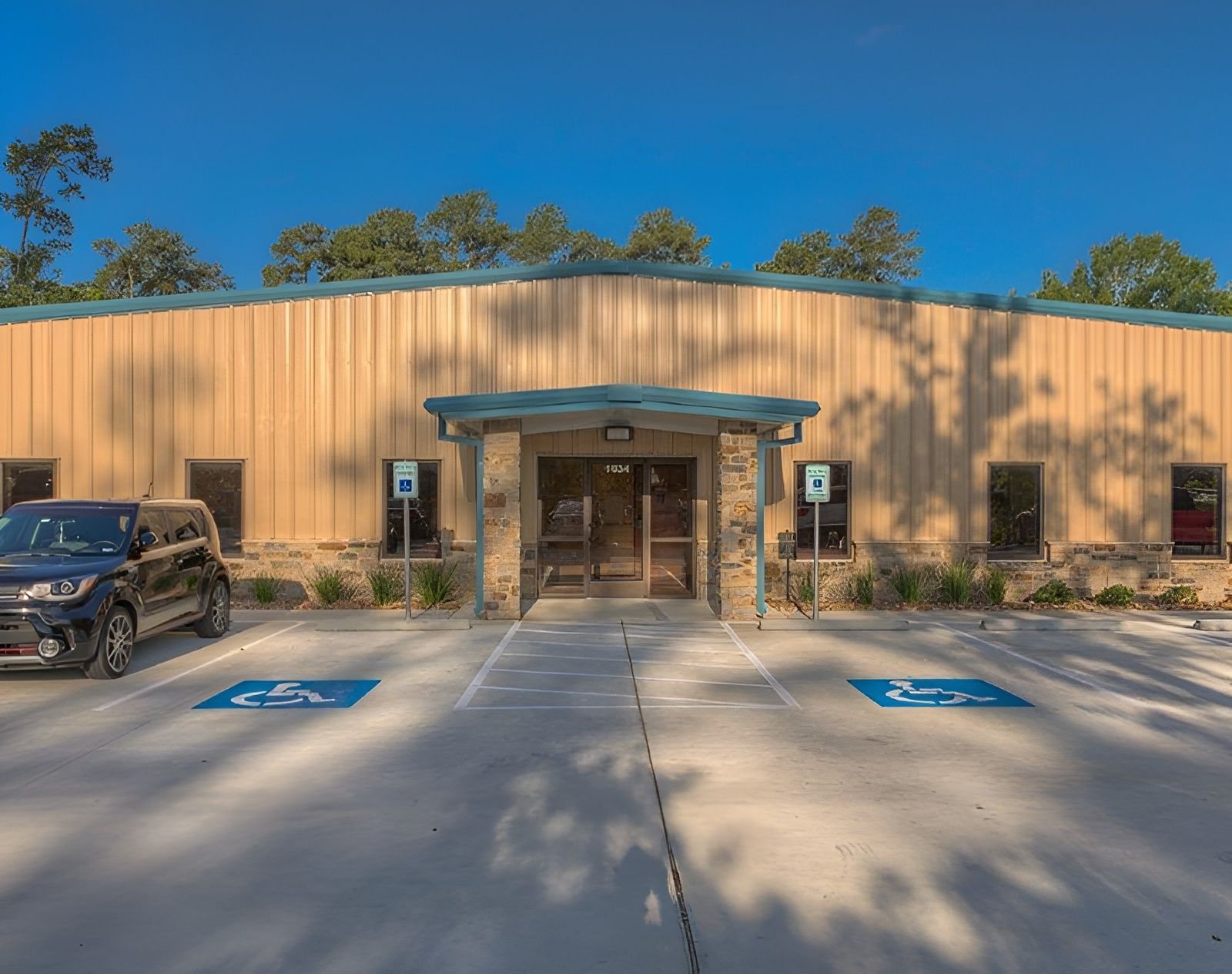 Tan building with accessible parking and stone entrance. SUV parked to the left.