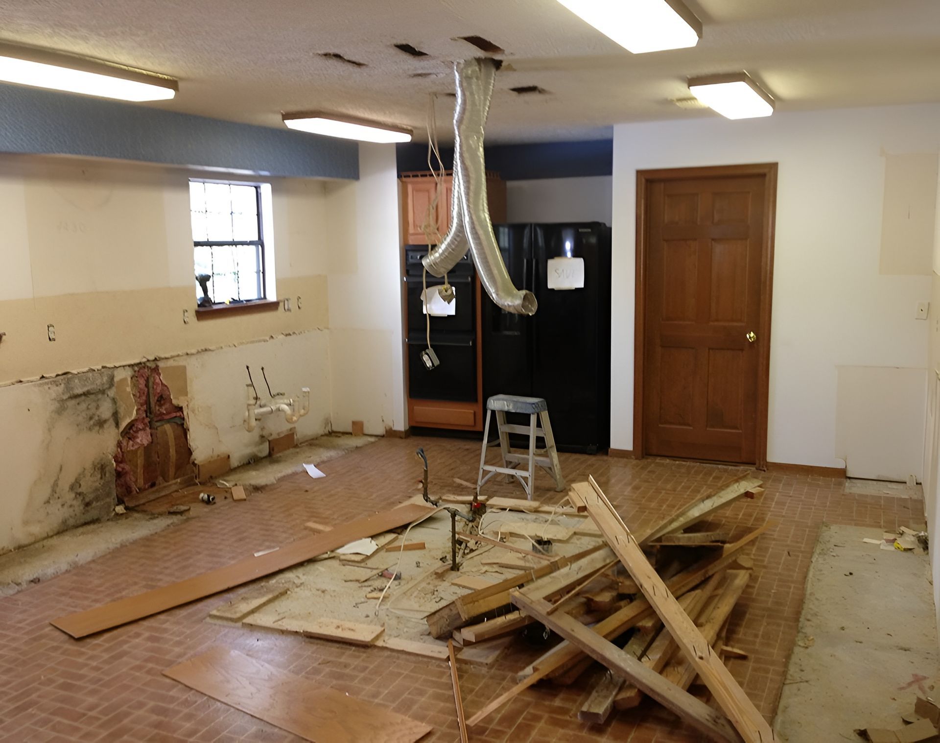Kitchen renovation with exposed walls, debris on floor, and hanging ventilation.