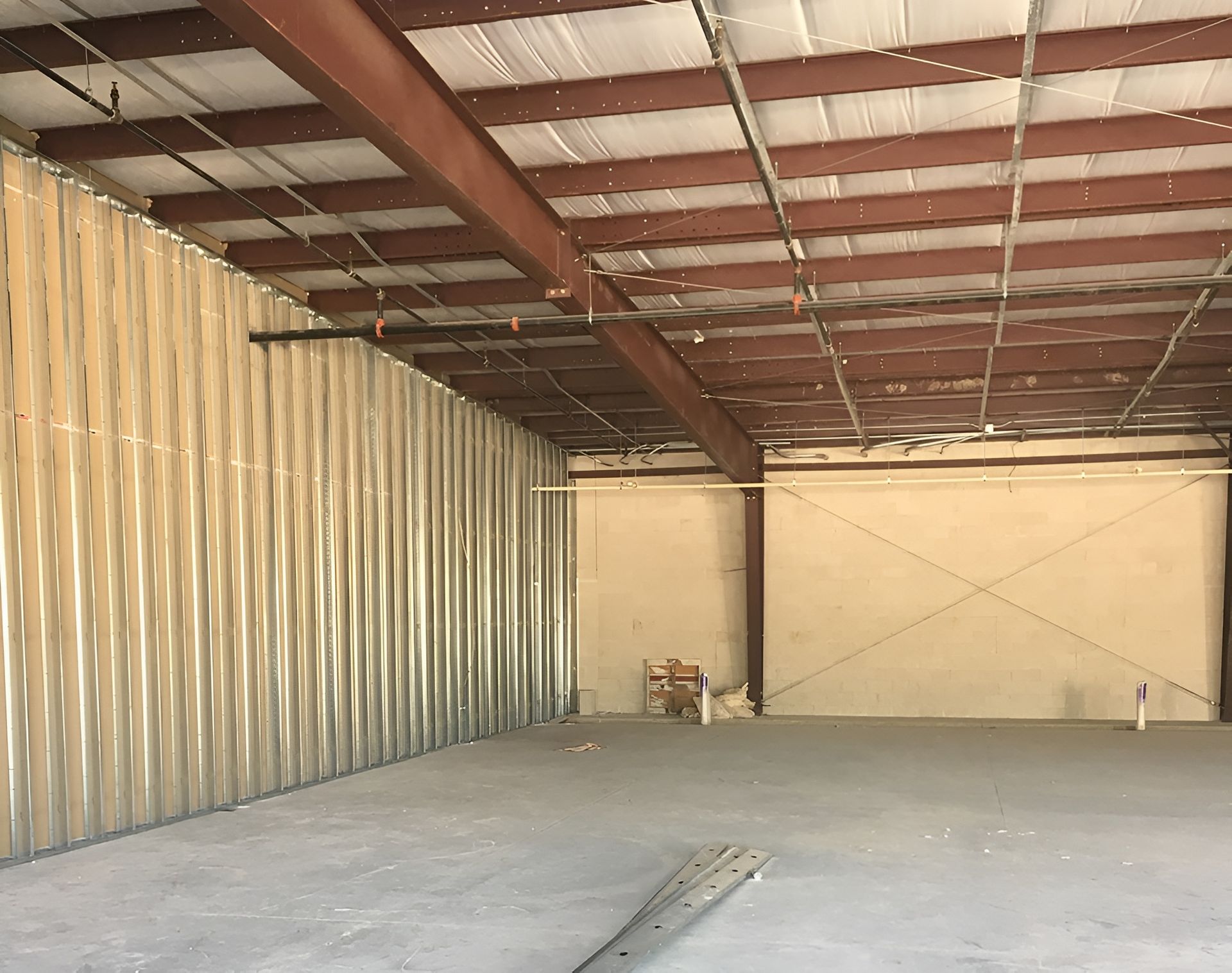 Interior view of an empty commercial building with corrugated metal walls and ceiling, concrete floor.