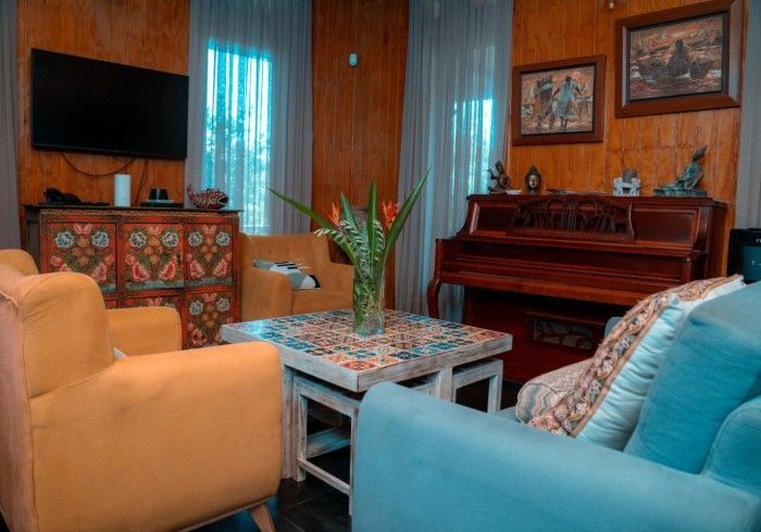A living room with a piano, blue and yellow armchairs, and a wooden coffee table with floral accents.