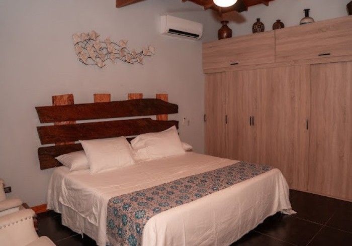 Bedroom with a wooden headboard, white bedding, and a large wooden closet. A decorative art piece hangs on the wall.