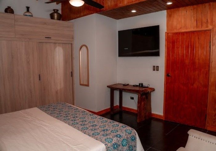 Bedroom with a light blue and white patterned bedspread, wooden furniture, a mounted TV, and a full-length mirror.