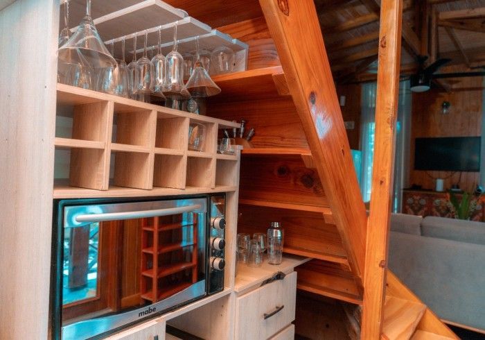 Wooden staircase with built-in storage and a small kitchen area. Includes an oven, wine rack, and hanging glasses.