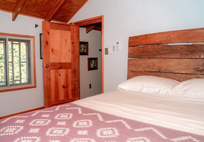 Bedroom with wooden headboard, door, and window. Bed has a purple patterned blanket.